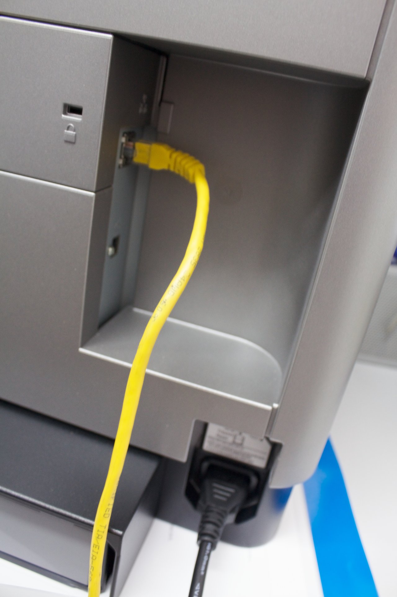 Photo of an Ethernet cable connected to the network port of an office laser printer, representing the network-exposed PaperCut print-management servers attackers are exploiting
